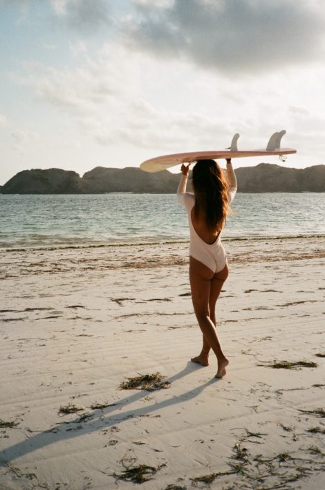 woman in white bikini holding white surfboard standing on beach during daytime
